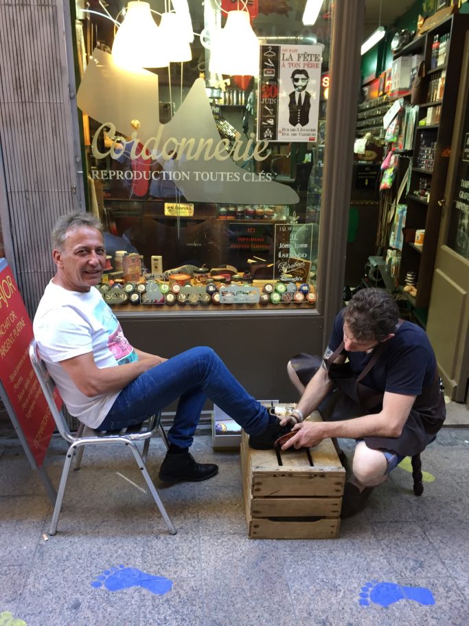 Atelier de cirage de chaussures devant la boutique Artisan cordonnier cirant des chaussures devant la boutique Au Louis XV à Perpignan